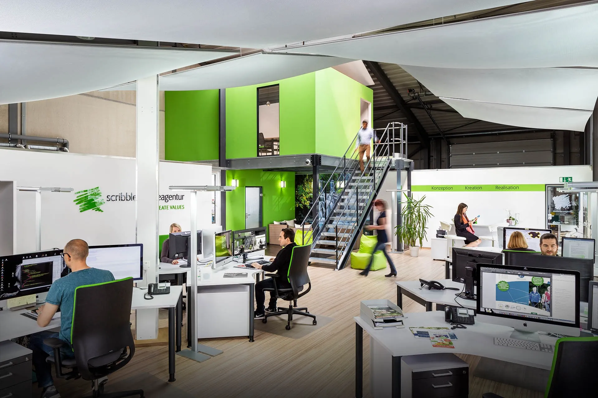 Das Studio der scribble Werbeagentur in Geilenkirchen: offener Arbeitsbereich mit Team, grüner Galerie und Scribble-Logo an der Wand